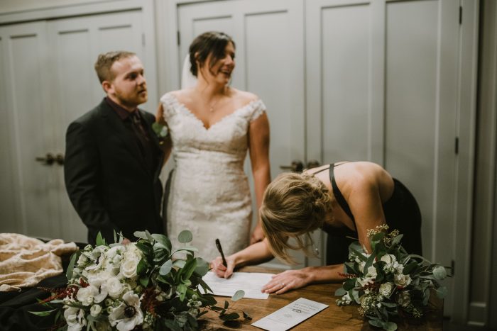 Maid of Honor signing the marriage license with bride and groom smiling