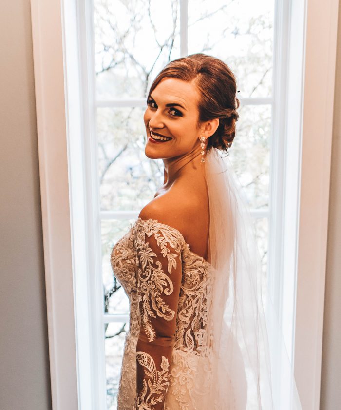 Bride looking back over her shoulder while standing in front of a full length window in the brides room