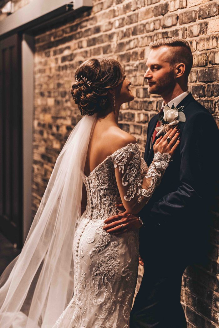 Groom leaning on an exposed brick wall with the bride leaning on his chest